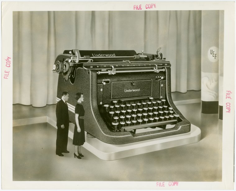 This image shows the scale of the typewriter with a man and woman standing next to it. Photo Credit: New York Public Library