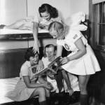 "Bunk room session: Gene George, 20, Peoria club member from Regina Saskatchewan, Can., leans over from top bunk to point to pix of catcher sister Bonnie Baker in a Sport magazine, l-r: Daisy Junor, 27, South Bend, Ind., club from Regina, Can.; Dorice Reid, 19, Superior Wisc., Chicago club member; and Dodie Healy, 19, Stockton, Calif., Chicago club member." (Florida Memory)
