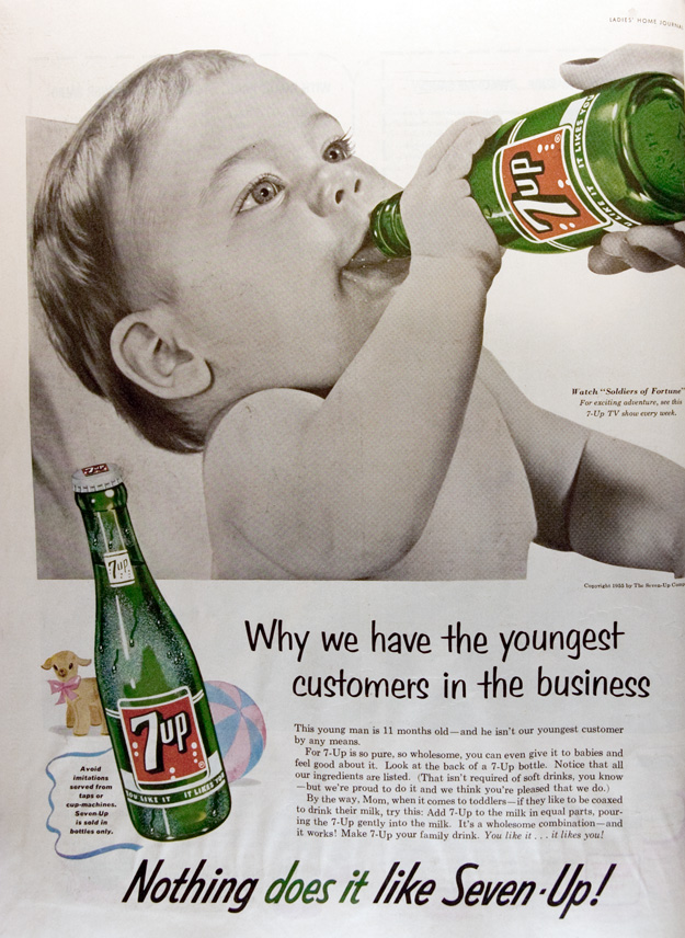 Advertisement for 7-Up soda. Depicts a baby drinking 7-up, while a woman's hand holds up the bottle for him to drink. 1955. 