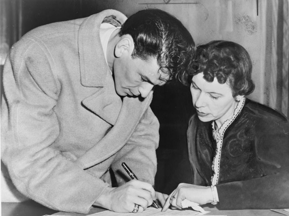 Frank Sinatra signs his induction papers while Chief Clerk Mrs. Mae E. Jones helps out at local board No. 19 on 160 Danforth St., Jersey City in 1943.